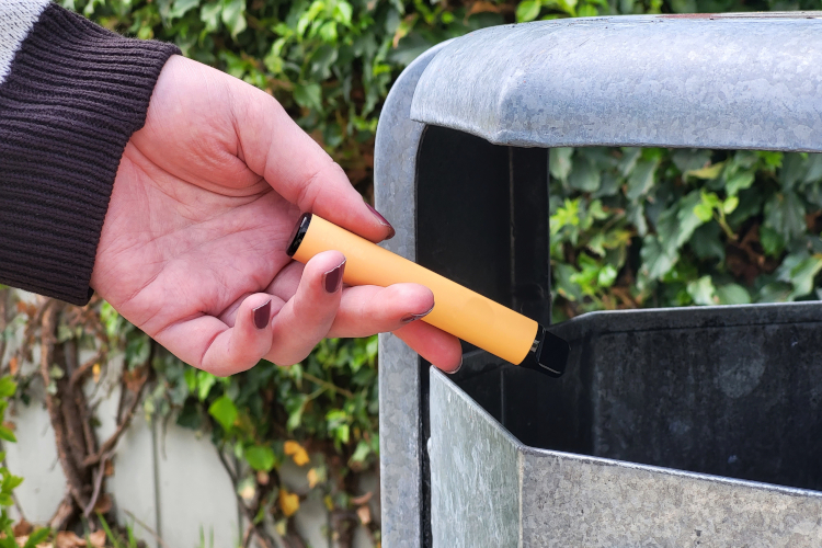 Eine Hand wirft eine verbrauchte Einweg-E-Zigarette in einen Abfalleimer